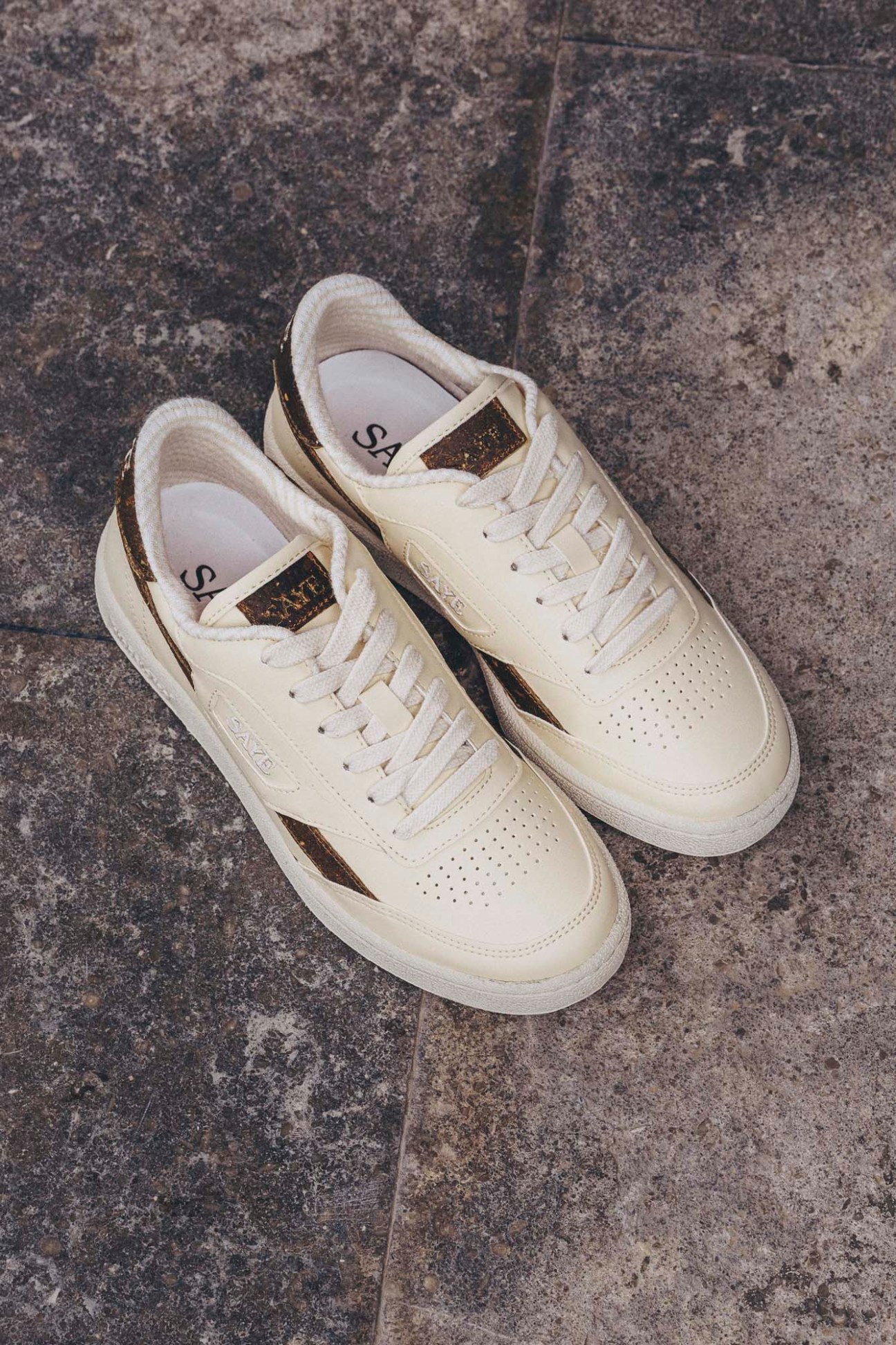 Saye's Modelo '89 white leather trainers with black and gold accents on concrete background.