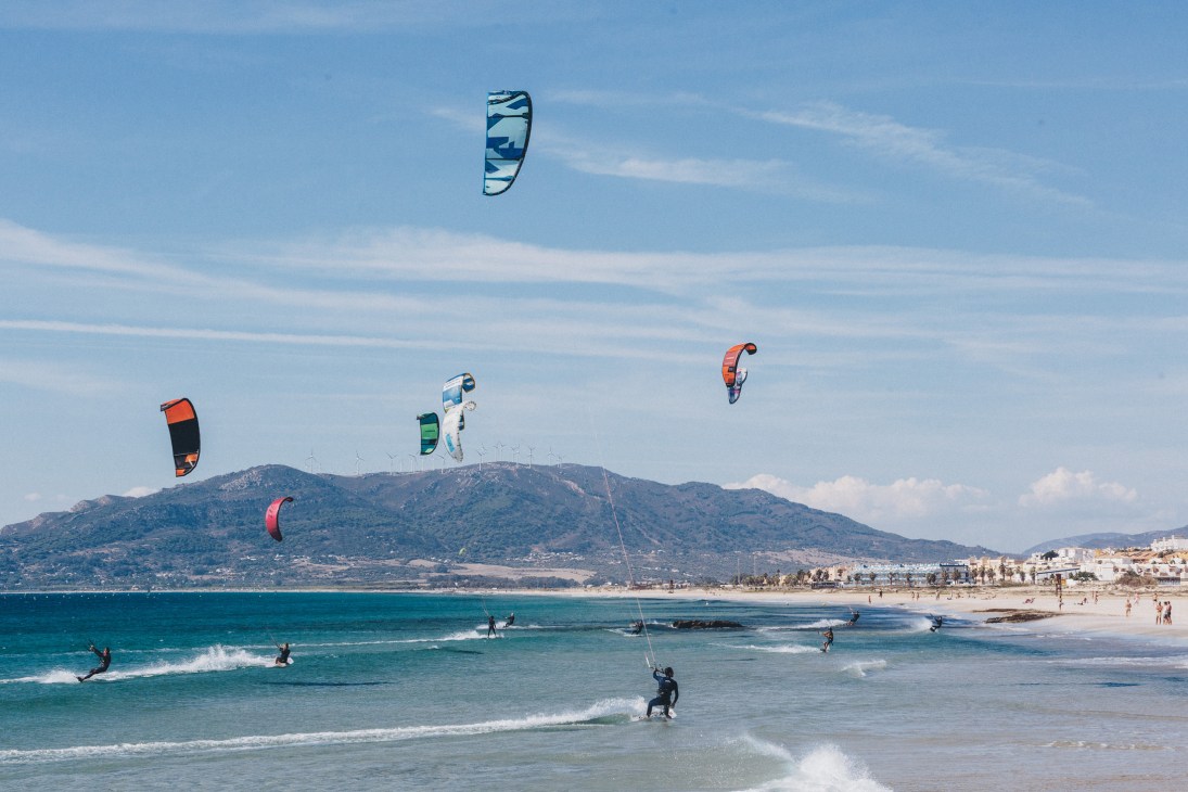 Kite surfers with colorful kites on Playa de los Lances beach in Tarifa with mountains in background.