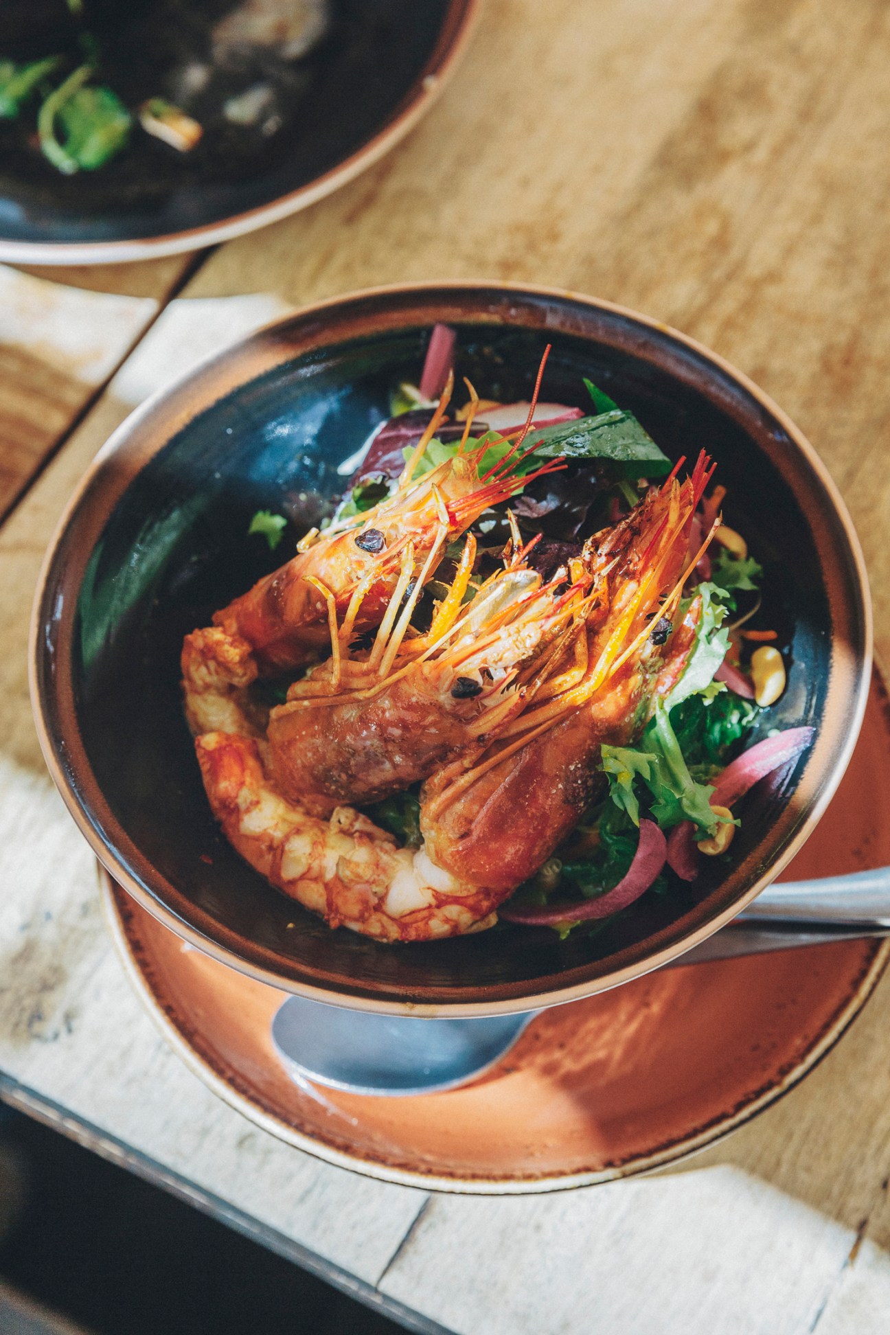 Grilled prawns with colorful garnish in a dark ceramic bowl at Bar El Francis restaurant.