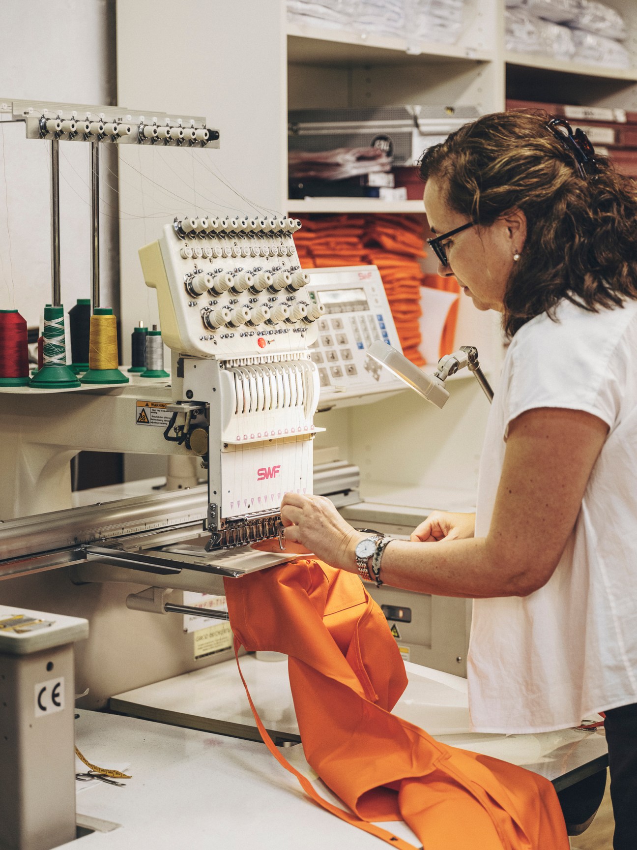 Woman in white shirt using embroidery machine to work on orange fabric in textile workshop