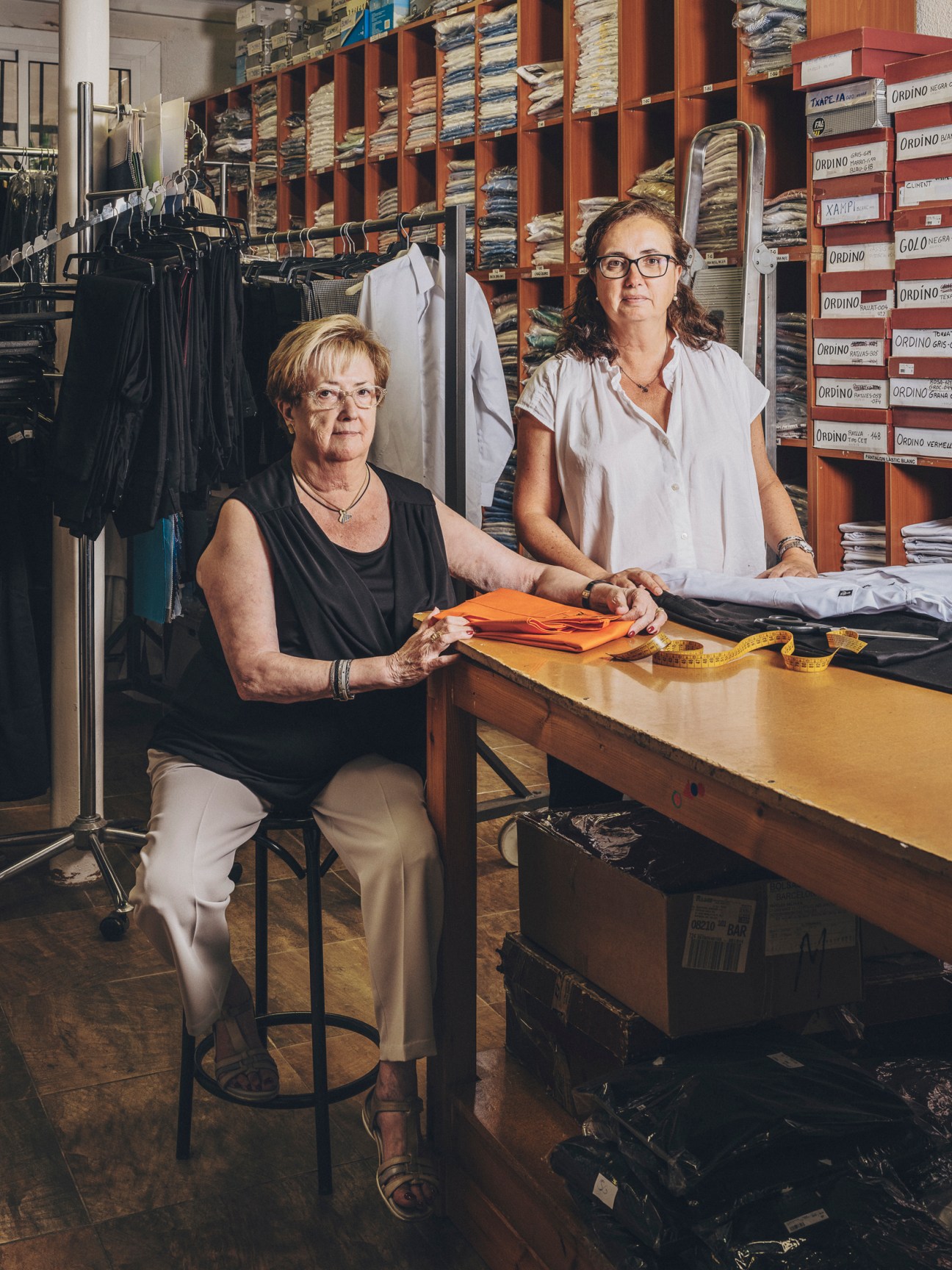 Two women standing together in traditional uniform shop, mother and daughter who run the family business