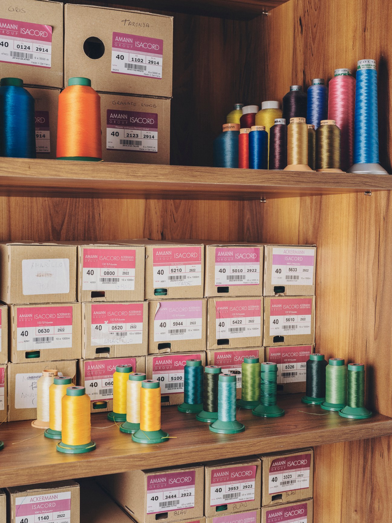 Organized shelves displaying colorful thread spools and boxes in a tailor's workshop storage area