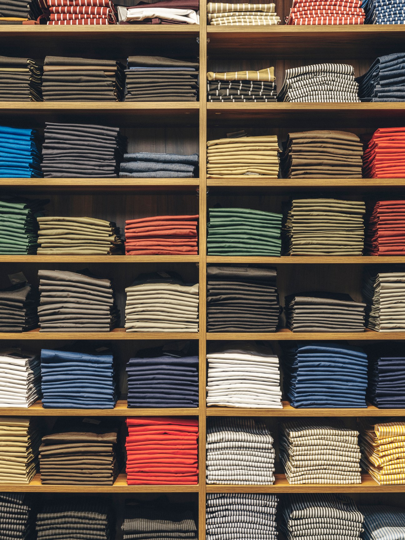 Neatly organized shelves displaying folded hospitality uniforms in various colors including chef jackets and aprons