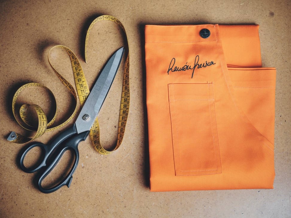 Orange fabric pieces with measuring tape and scissors arranged on work surface for garment construction