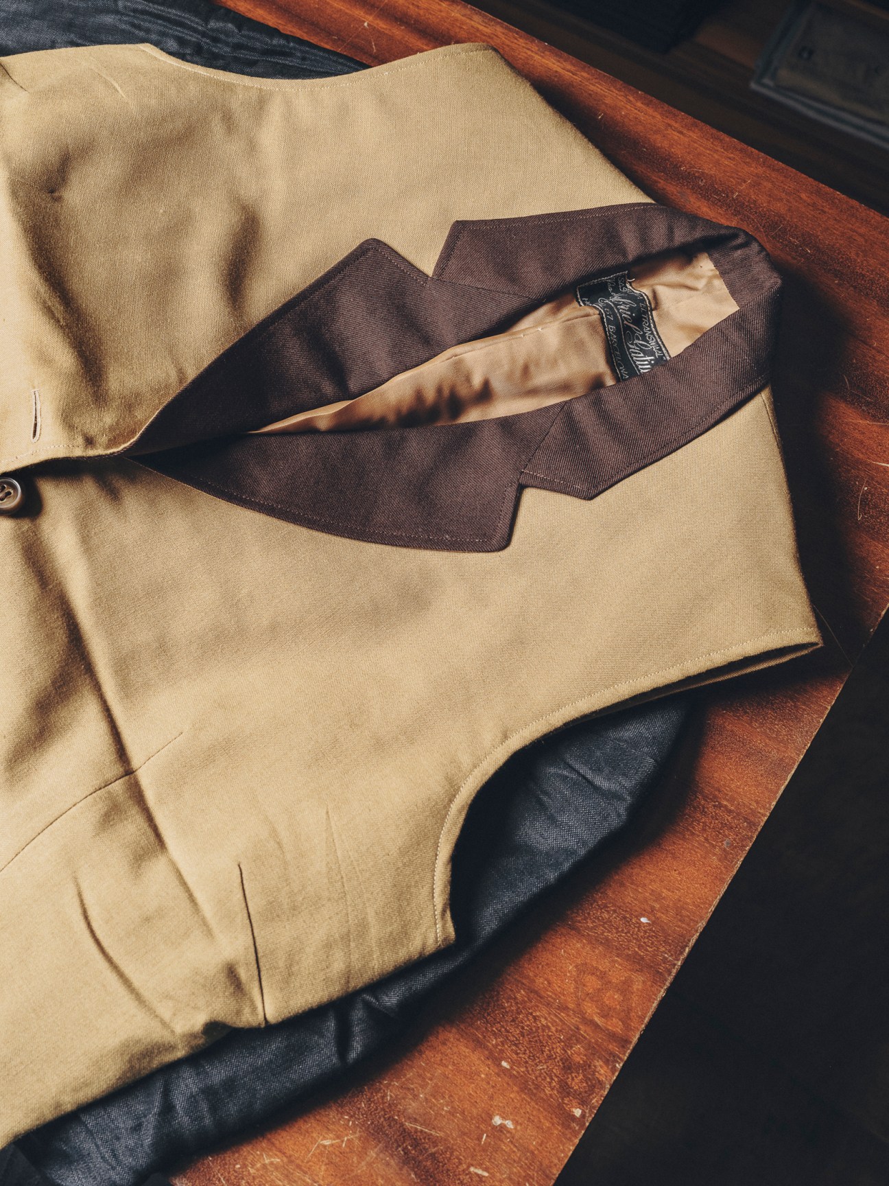 Beige waiter's jacket with brown collar and trim displayed on wooden chair