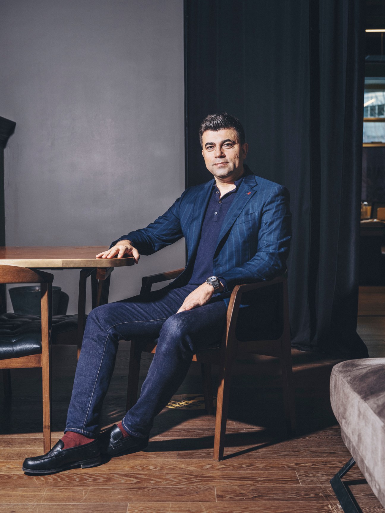 Kemal Erol, founder of Vivense, sitting in a chair wearing a navy suit in a modern interior setting