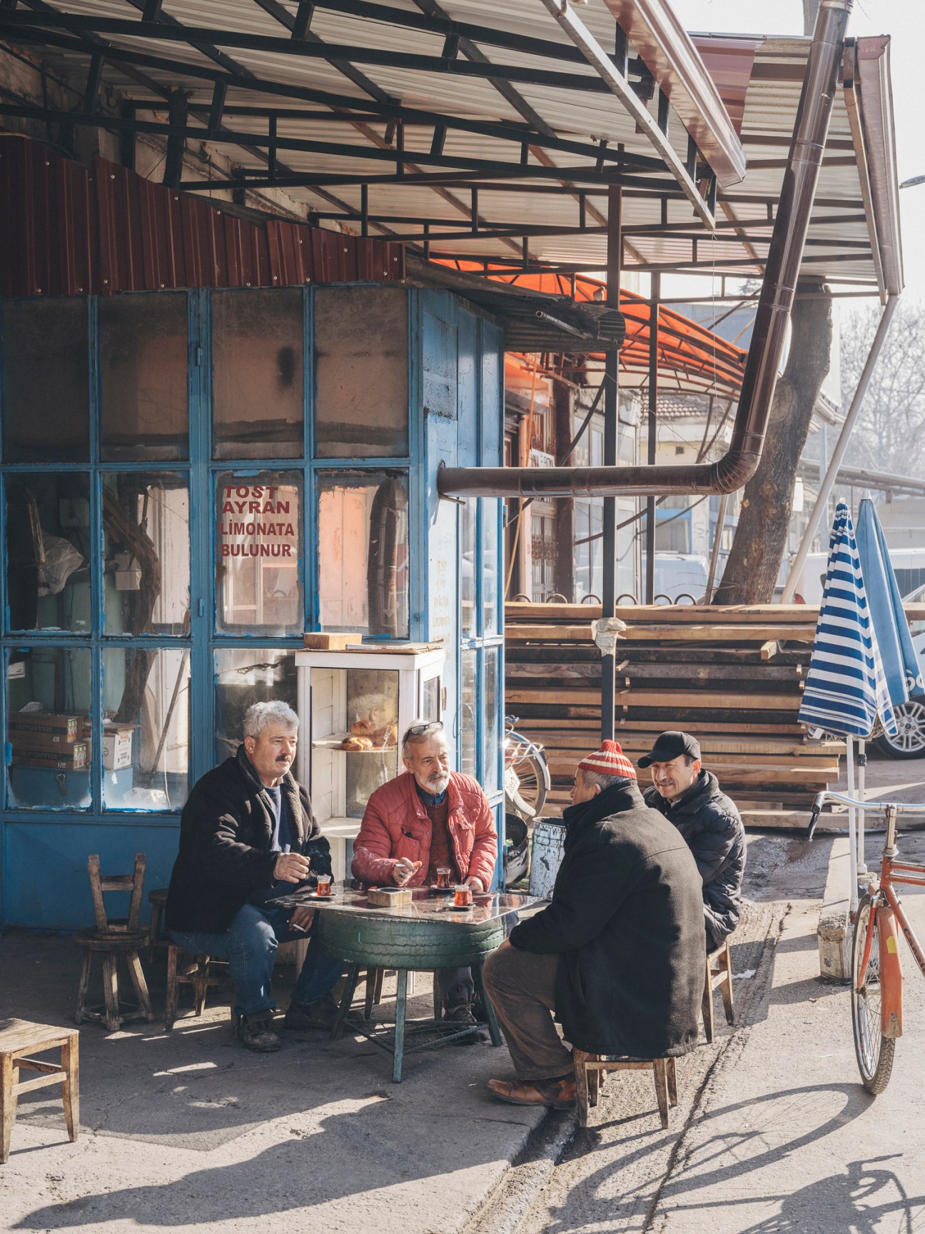 Four men sitting around a small table having tea outside a traditional workshop with blue wooden doors