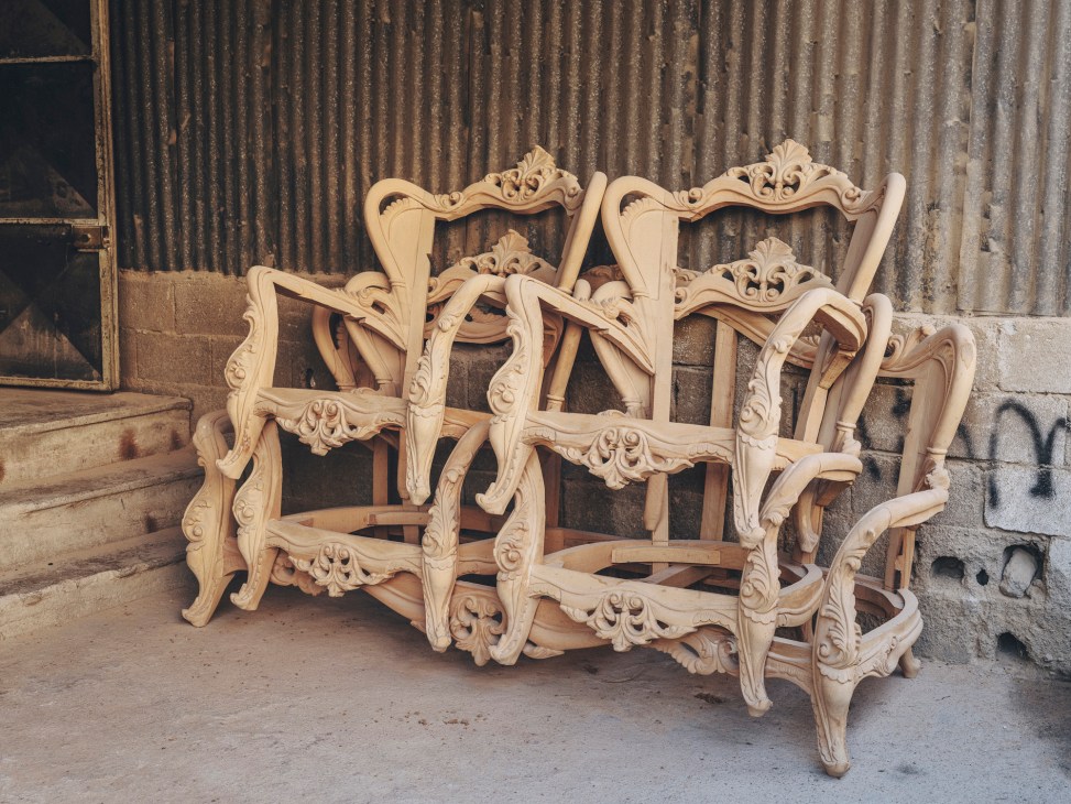 Ornate wooden chair frames with decorative carved details stacked in a furniture workshop
