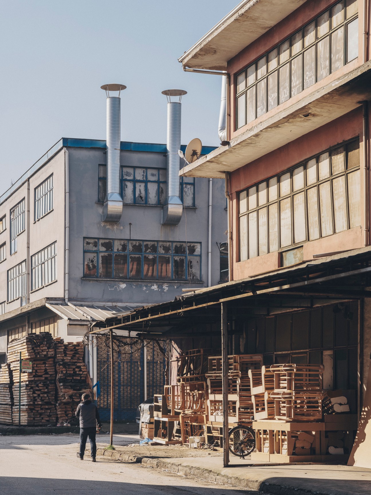Industrial buildings with metal chimneys and wooden materials stacked outside furniture workshops in Inegöl