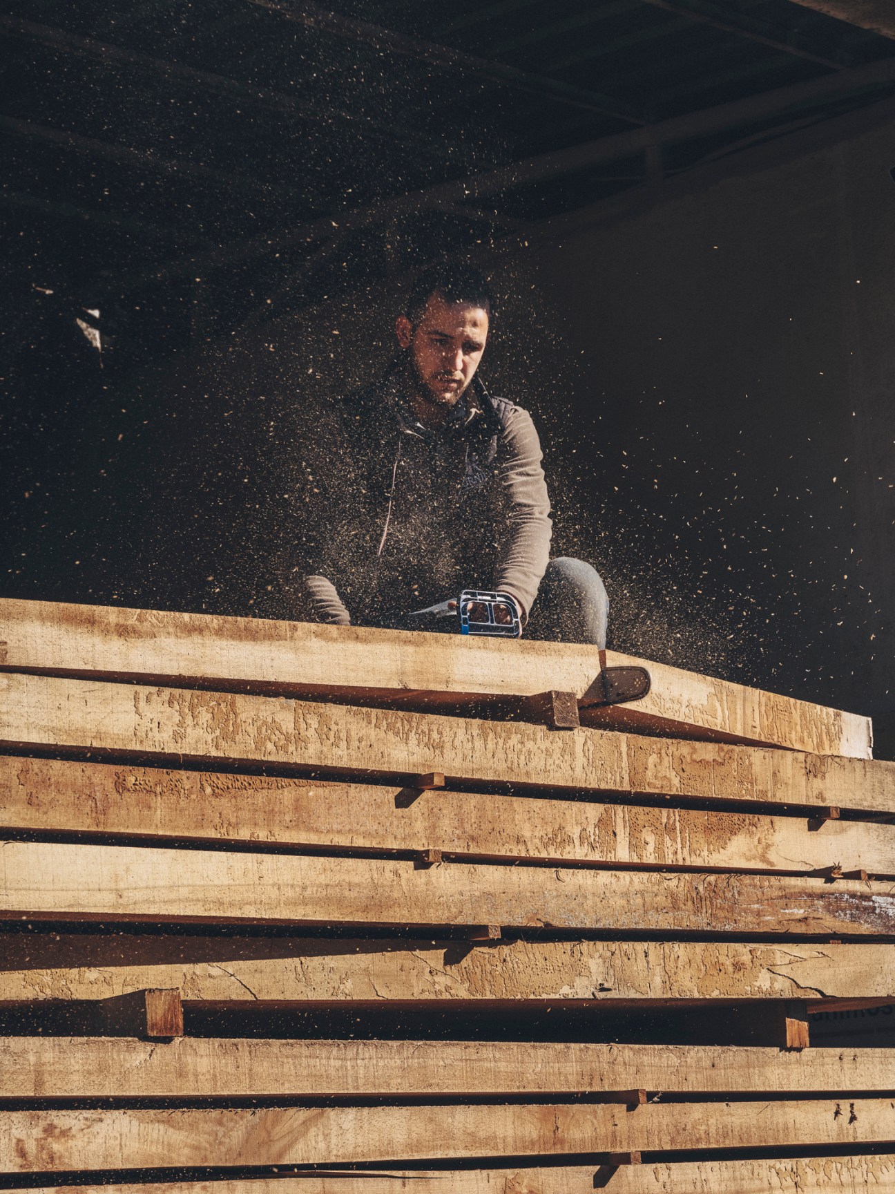 Worker in a furniture workshop surrounded by sawdust and wood particles in the air