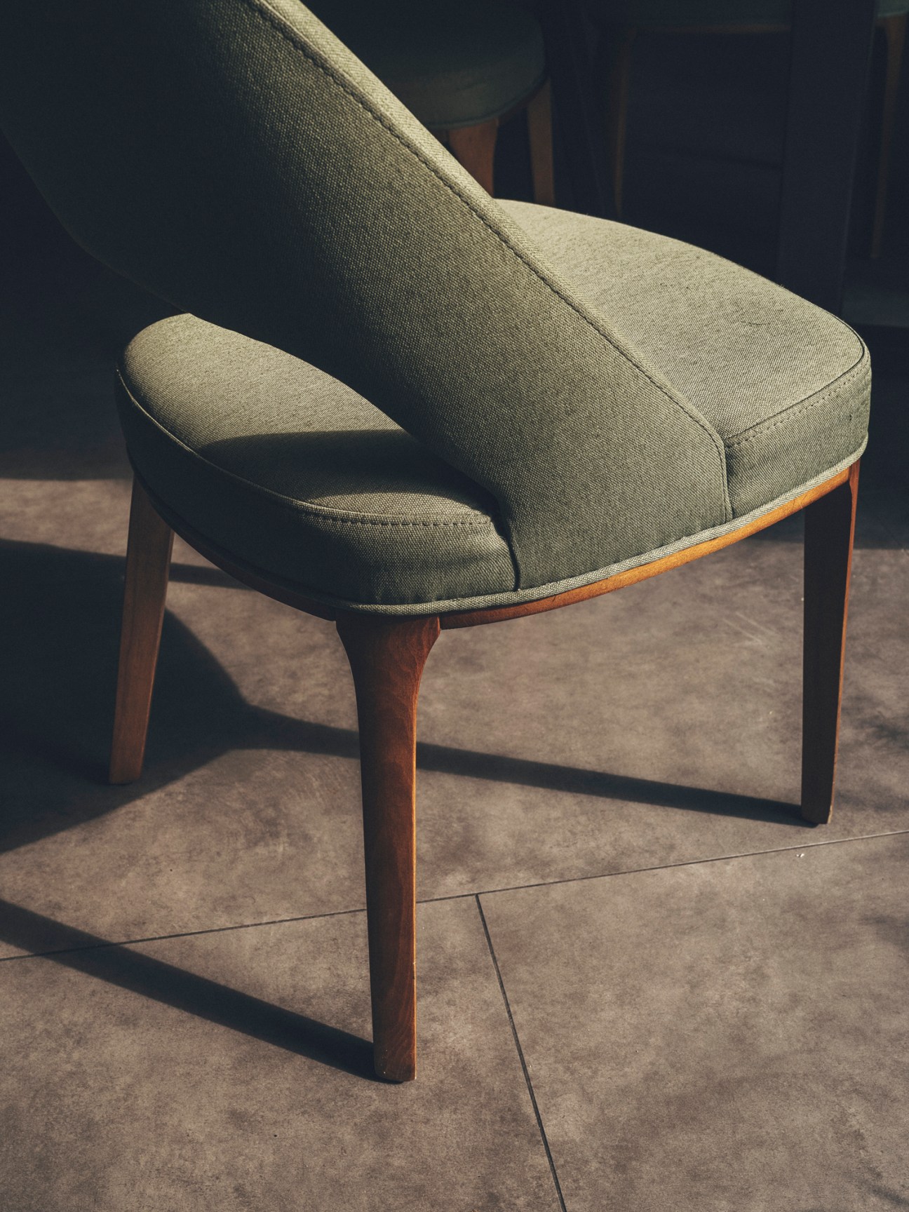 Gray upholstered mid-century style armchair with wooden legs on concrete floor