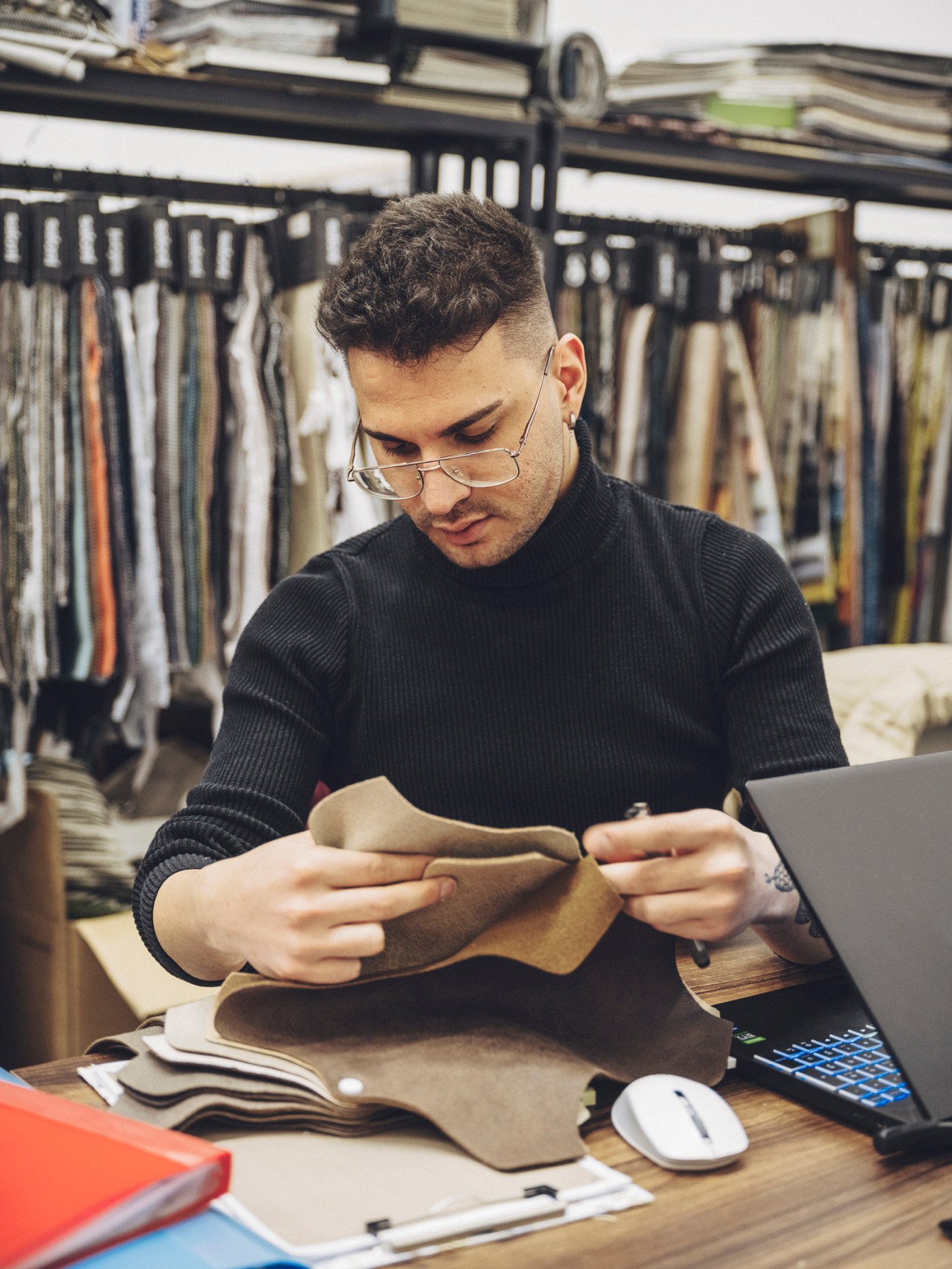 Onur Portakal examining leather material in a furniture workshop surrounded by fabric samples
