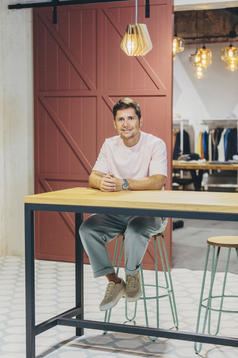 Rafa Gómez, co-founder of Unfeigned, sitting at a wooden table in a retail space with a terracotta wall backdrop.
