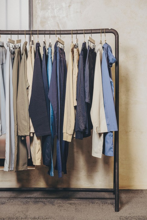 Clothing rack displaying neutral-toned basics including cream, navy, and blue garments hanging on wooden hangers.