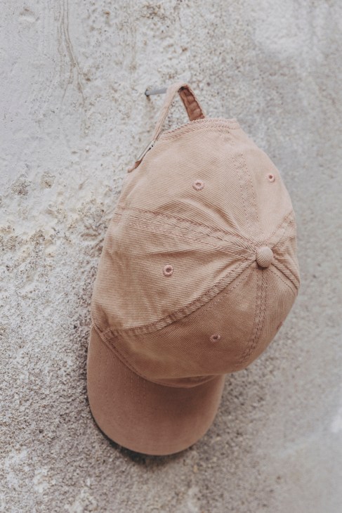 Unfeigned's Permanent baseball cap in cream lying on a textured concrete surface.