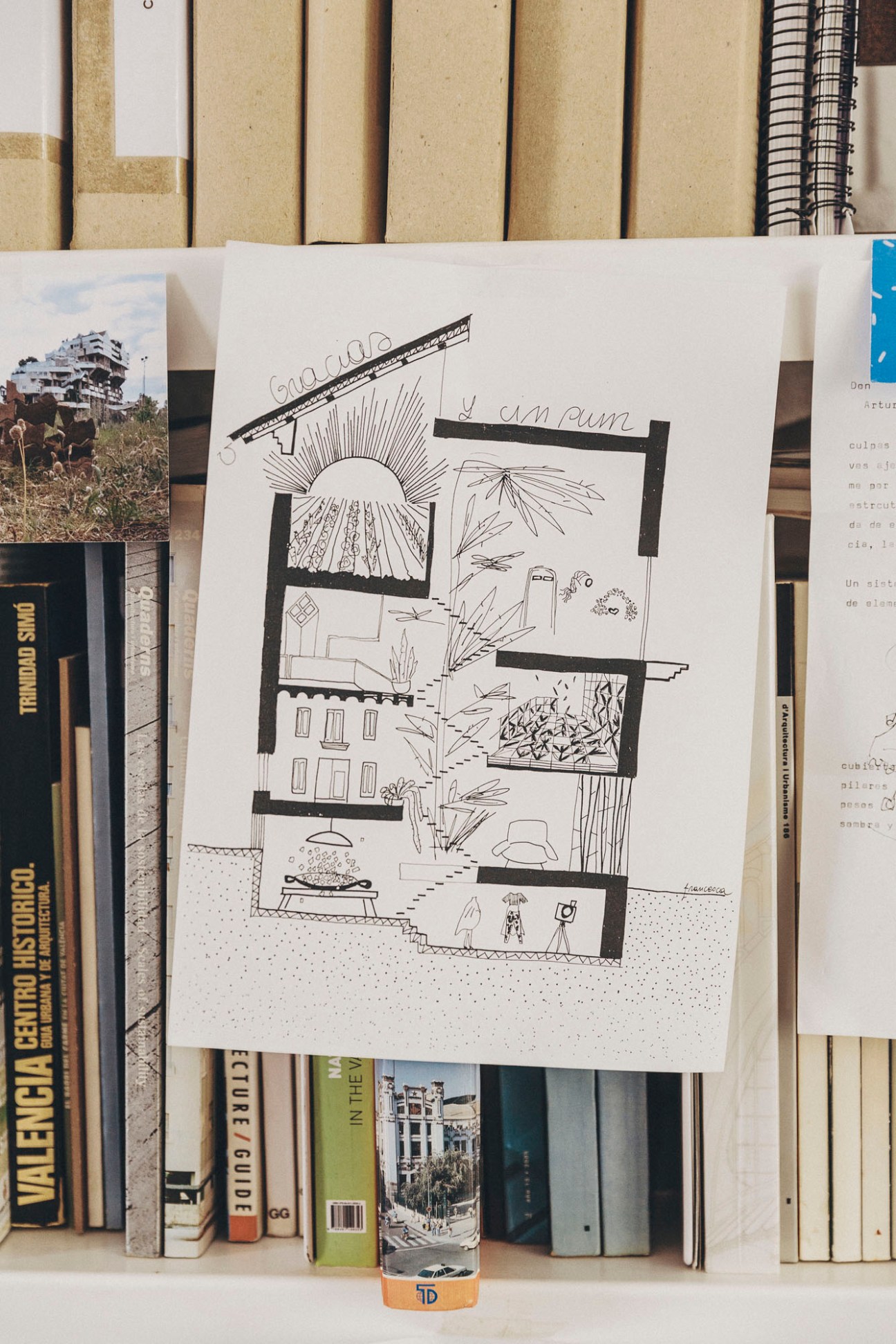 Hand-drawn architectural sketch showing cross-section of multi-story building with sun, displayed among books on shelf