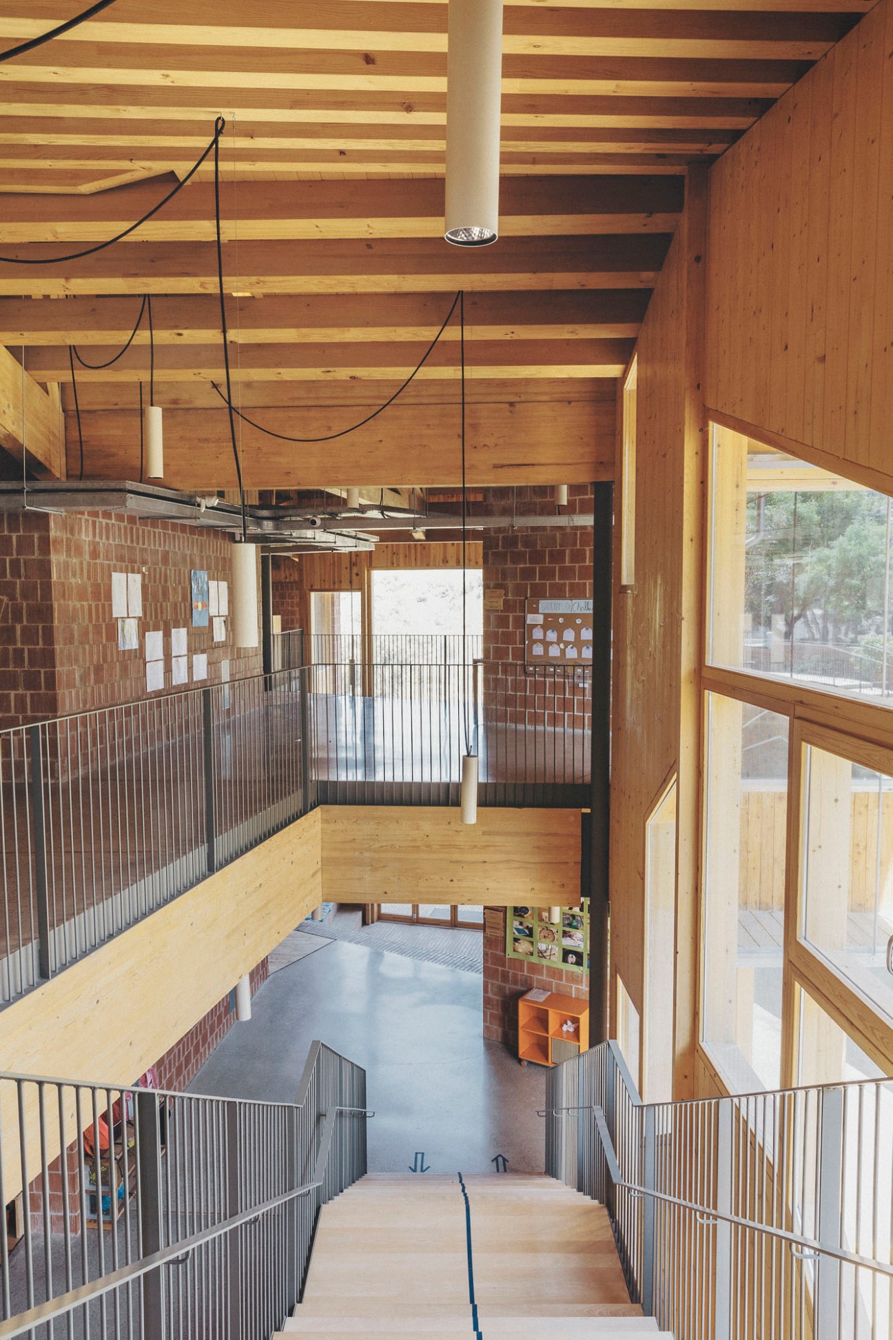 Interior staircase with exposed wooden ceiling beams, brick walls, metal railings and large windows