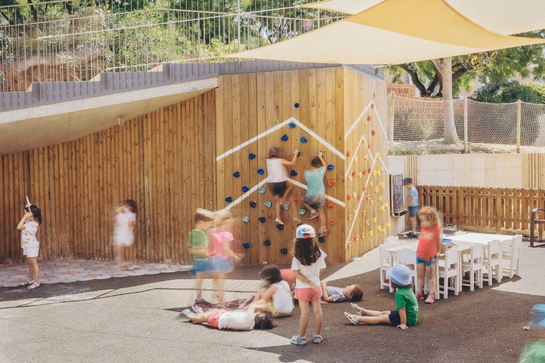 Children playing on outdoor wooden climbing wall and around playground area at school