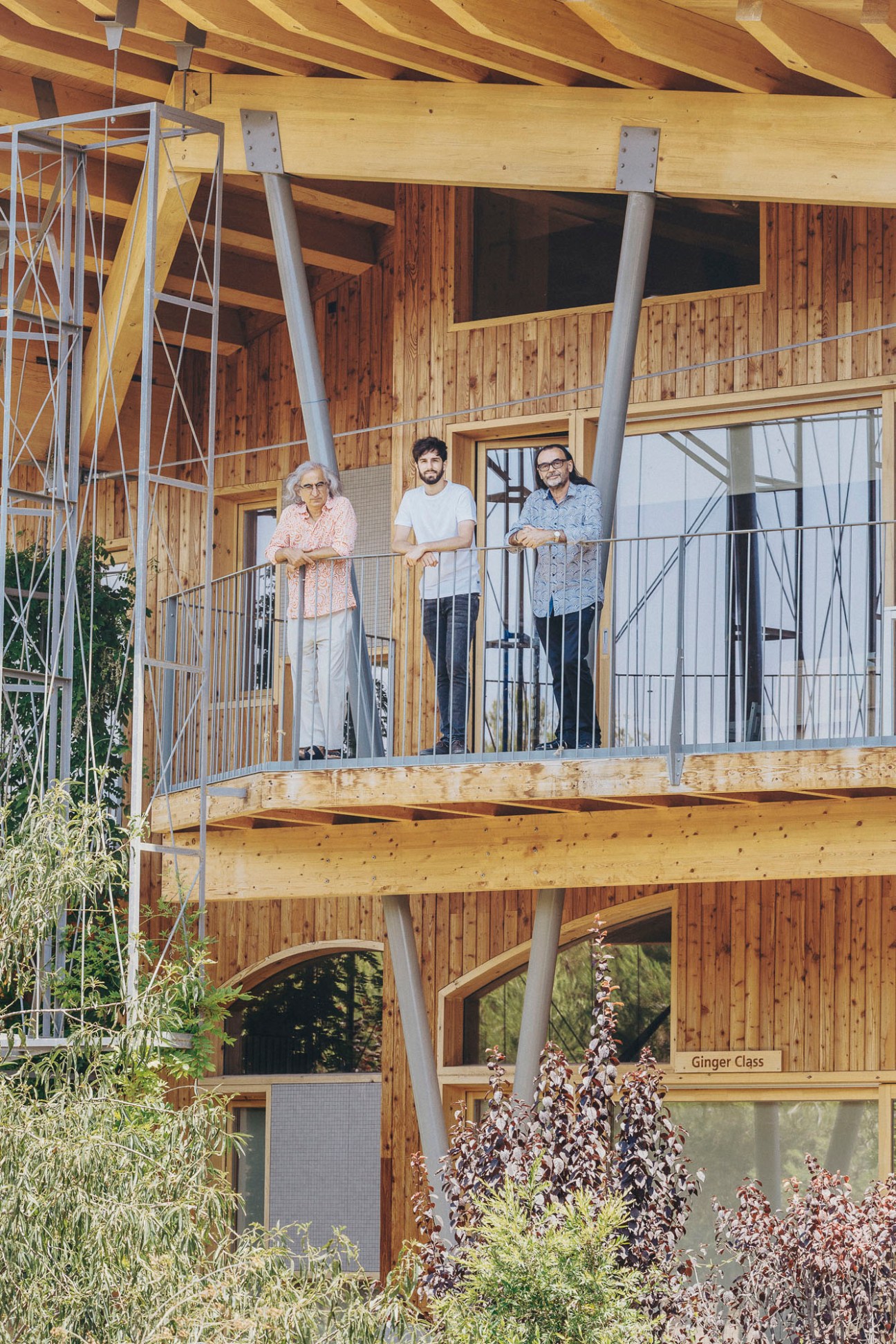 Three architects Arturo Sanz, Francisco López, and Carmel Gradolí standing on wooden balcony of timber building
