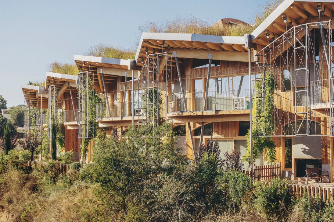 Modern residential buildings with wooden construction, green roofs, and glass balconies integrated into natural landscape