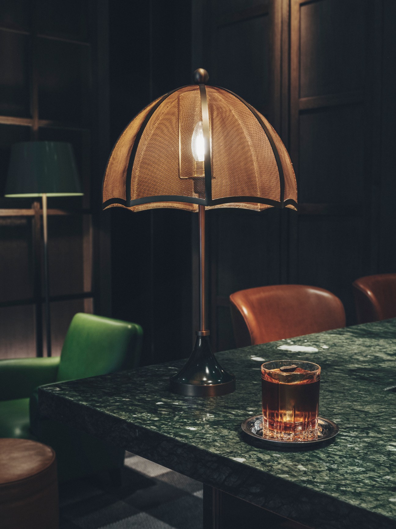 Elegant table lamp with woven dome shade illuminating whiskey glass on marble surface in upscale bar setting