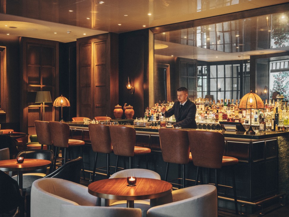 Bartender in dark suit working behind an elegant bar with extensive bottle display and warm amber lighting