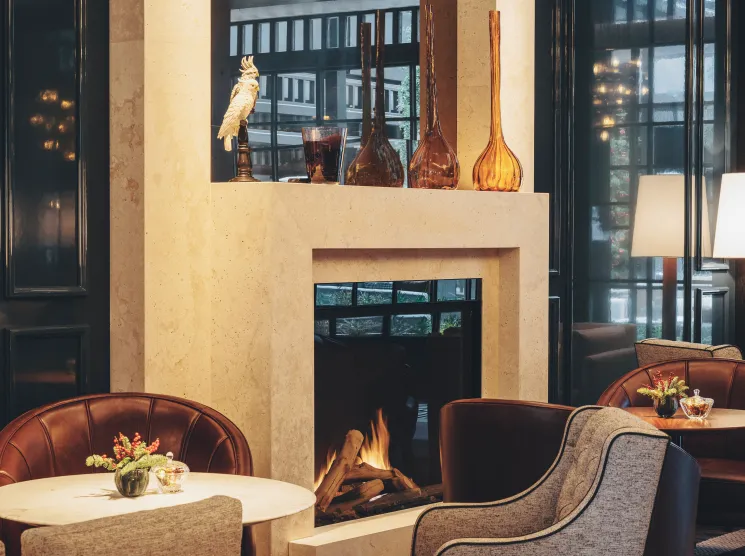 Elegant hotel lounge with fireplace, upholstered chairs, and decorative vases on mantel