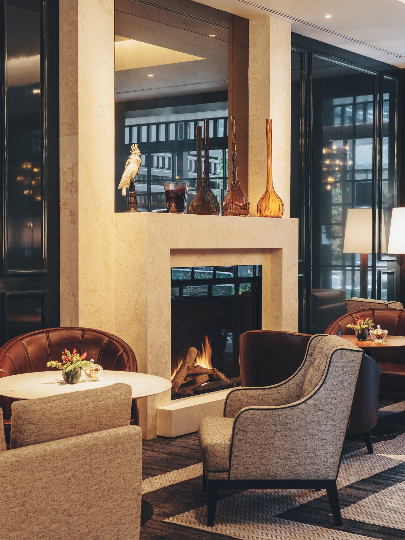 Elegant hotel lounge with fireplace, upholstered chairs, and decorative vases on mantel