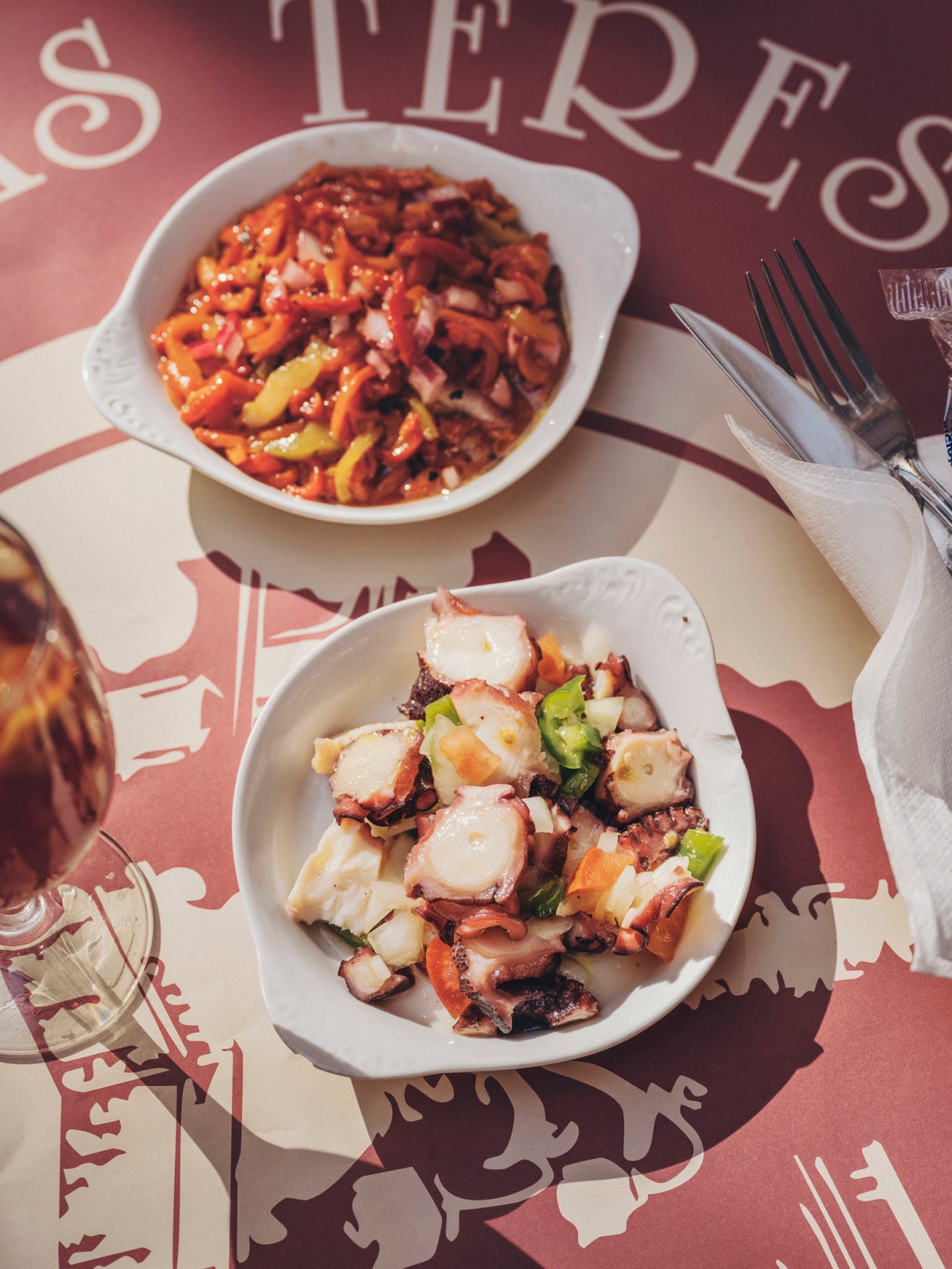 Two small white plates with Spanish tapas dishes on a red table with decorative text