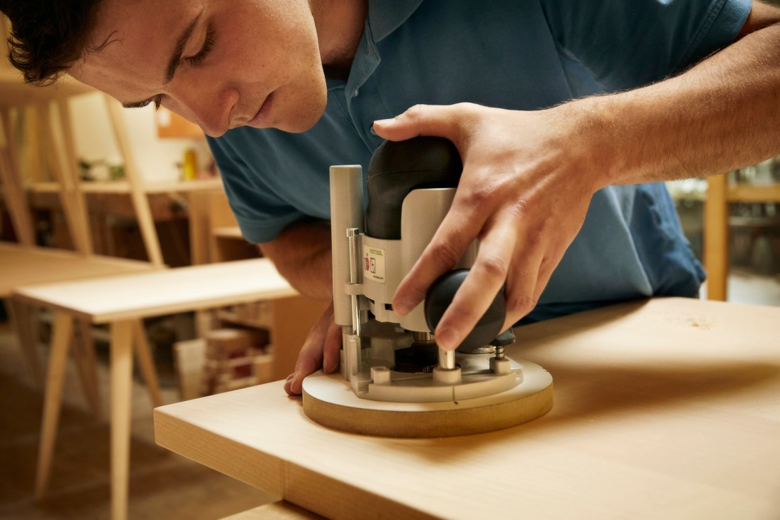 Person operating a precision router tool on a wooden workpiece in a furniture workshop