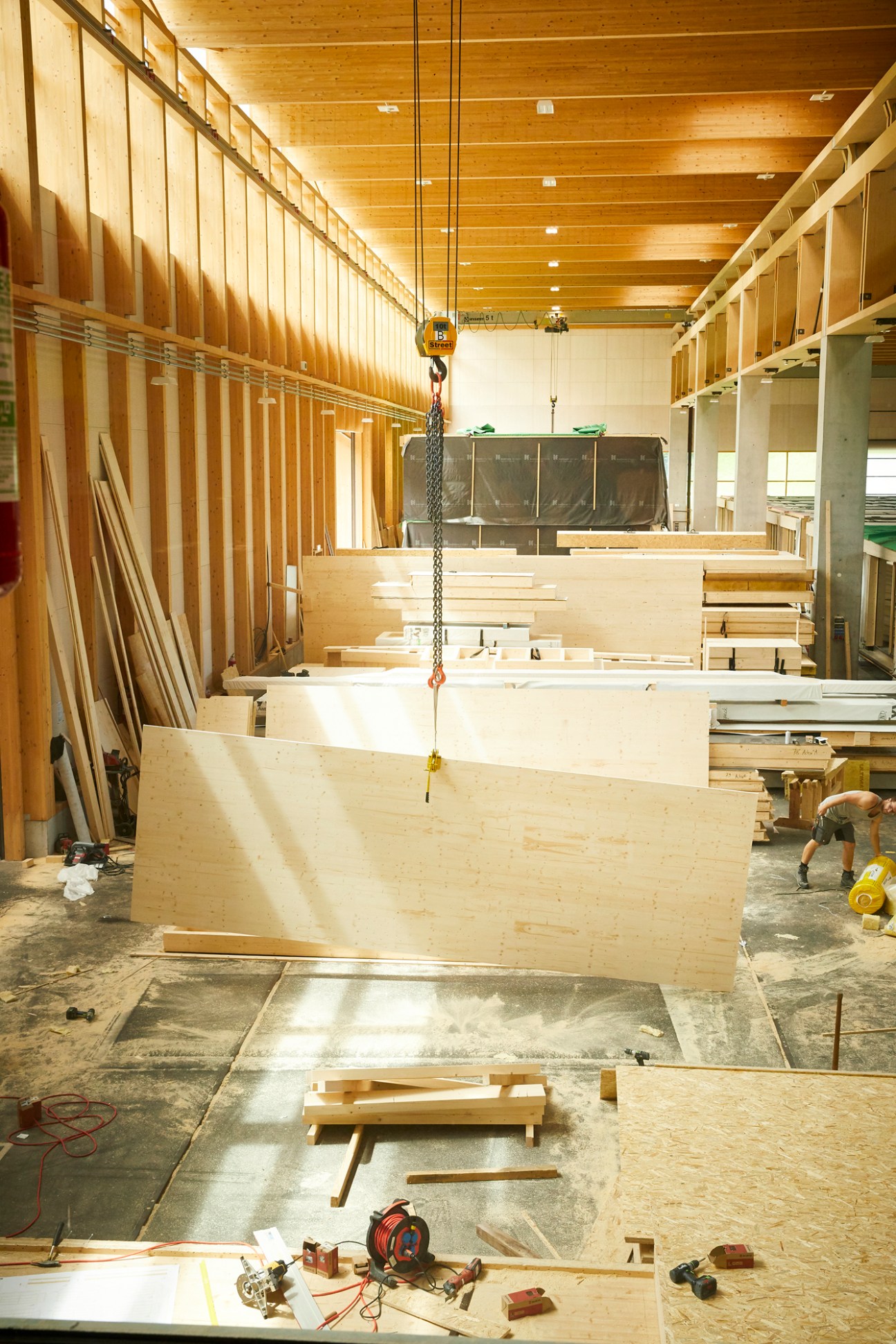 Large wooden modular building components suspended by crane chain in timber construction workshop