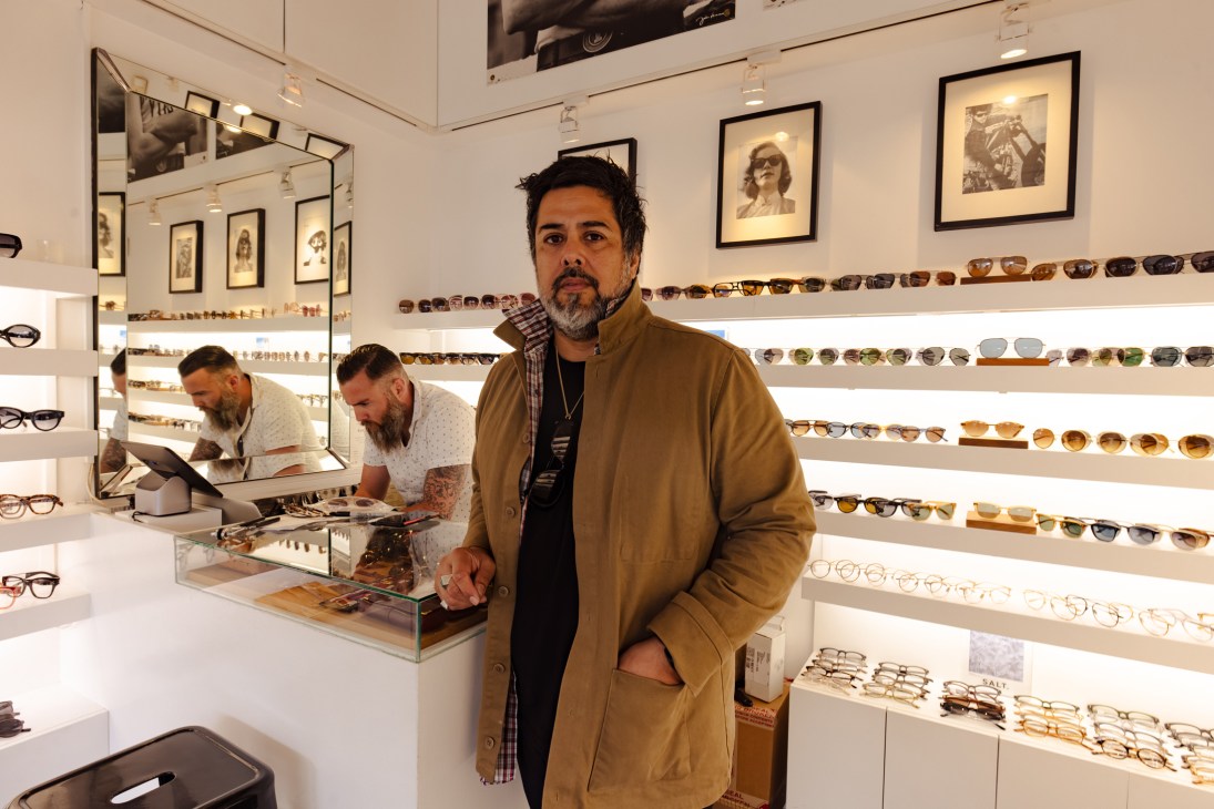 Man in tan coat standing in eyewear store with sunglasses displays on white shelves