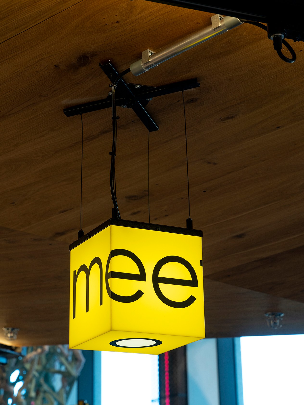 Yellow cube-shaped pendant light with black text hanging from wooden ceiling