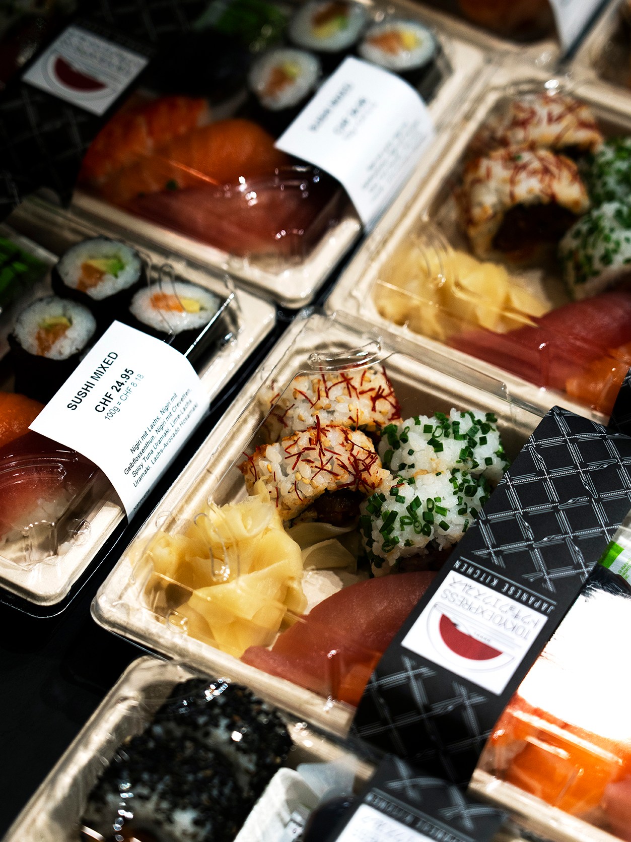 Multiple Japanese takeaway sushi boxes with labels displayed in clear plastic containers