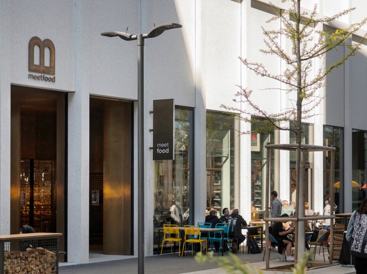 Modern concrete and glass building exterior with outdoor seating area and customers dining at tables