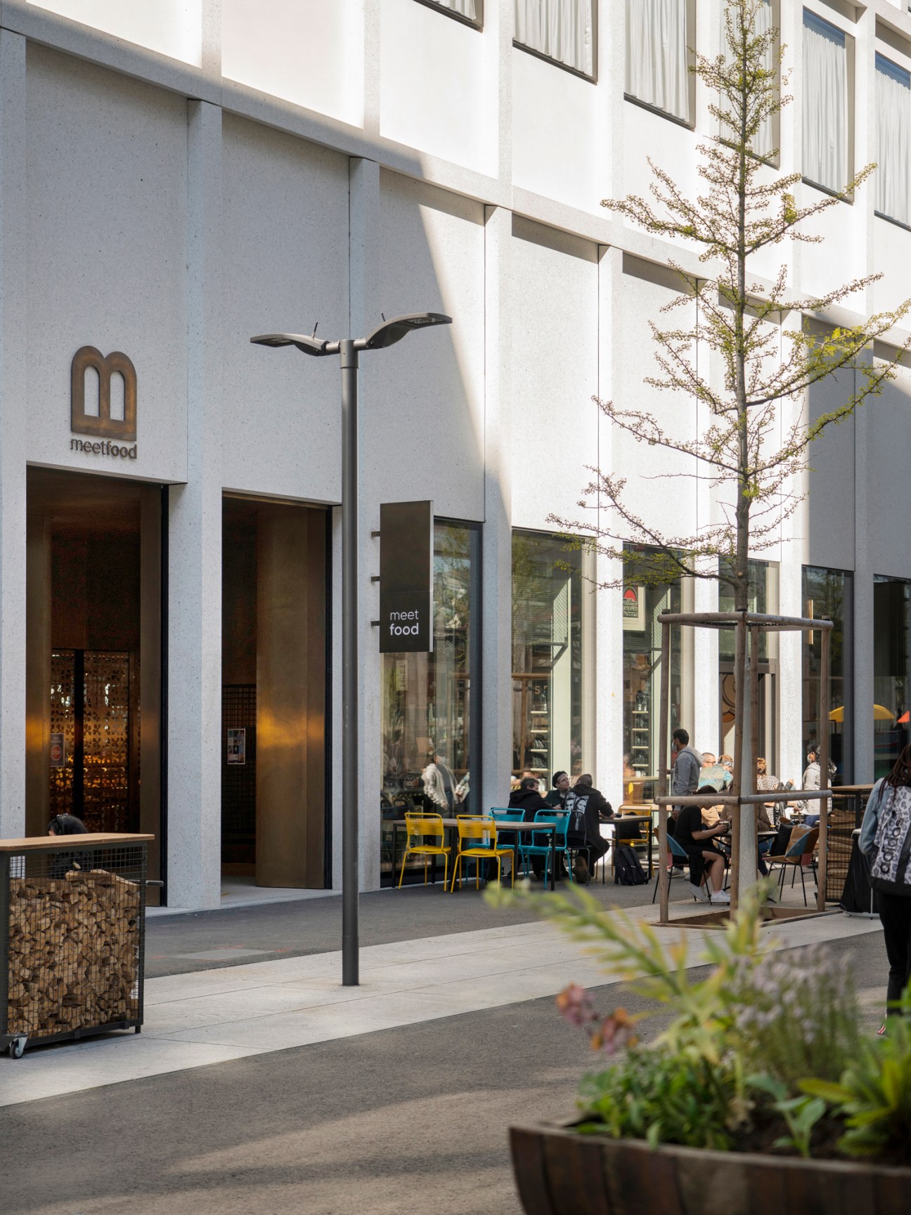 Modern concrete and glass building exterior with outdoor seating area and customers dining at tables
