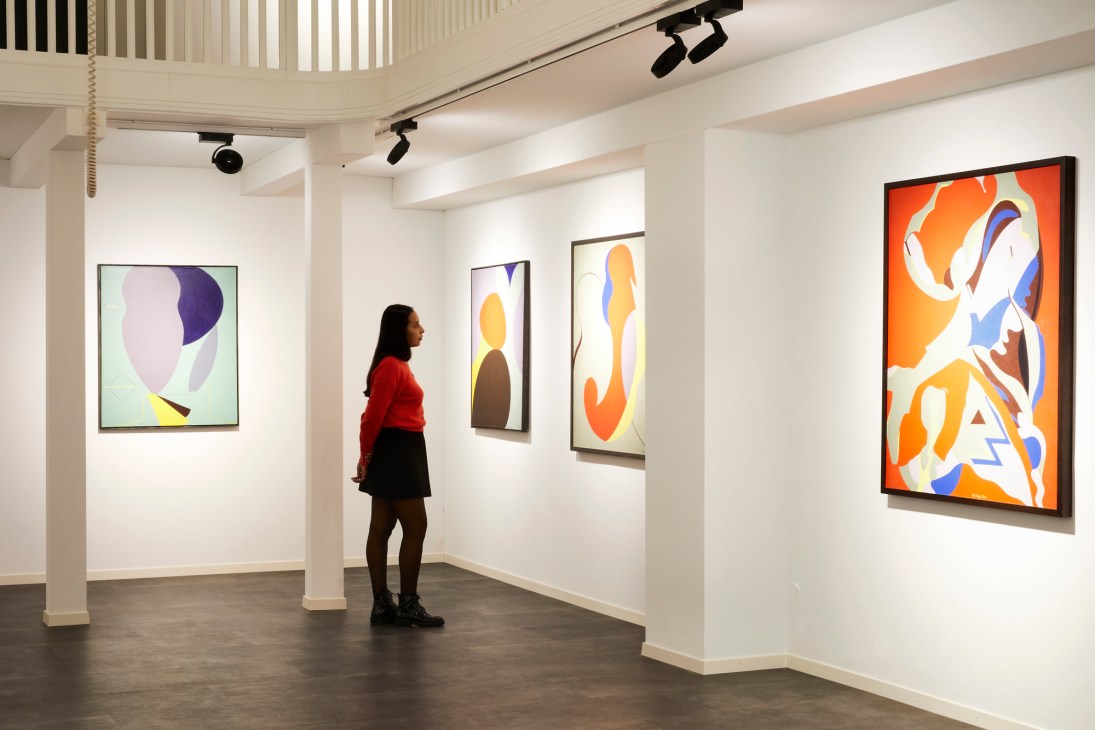 Gabriela Gonzalez standing in gallery space with colorful abstract paintings on white walls