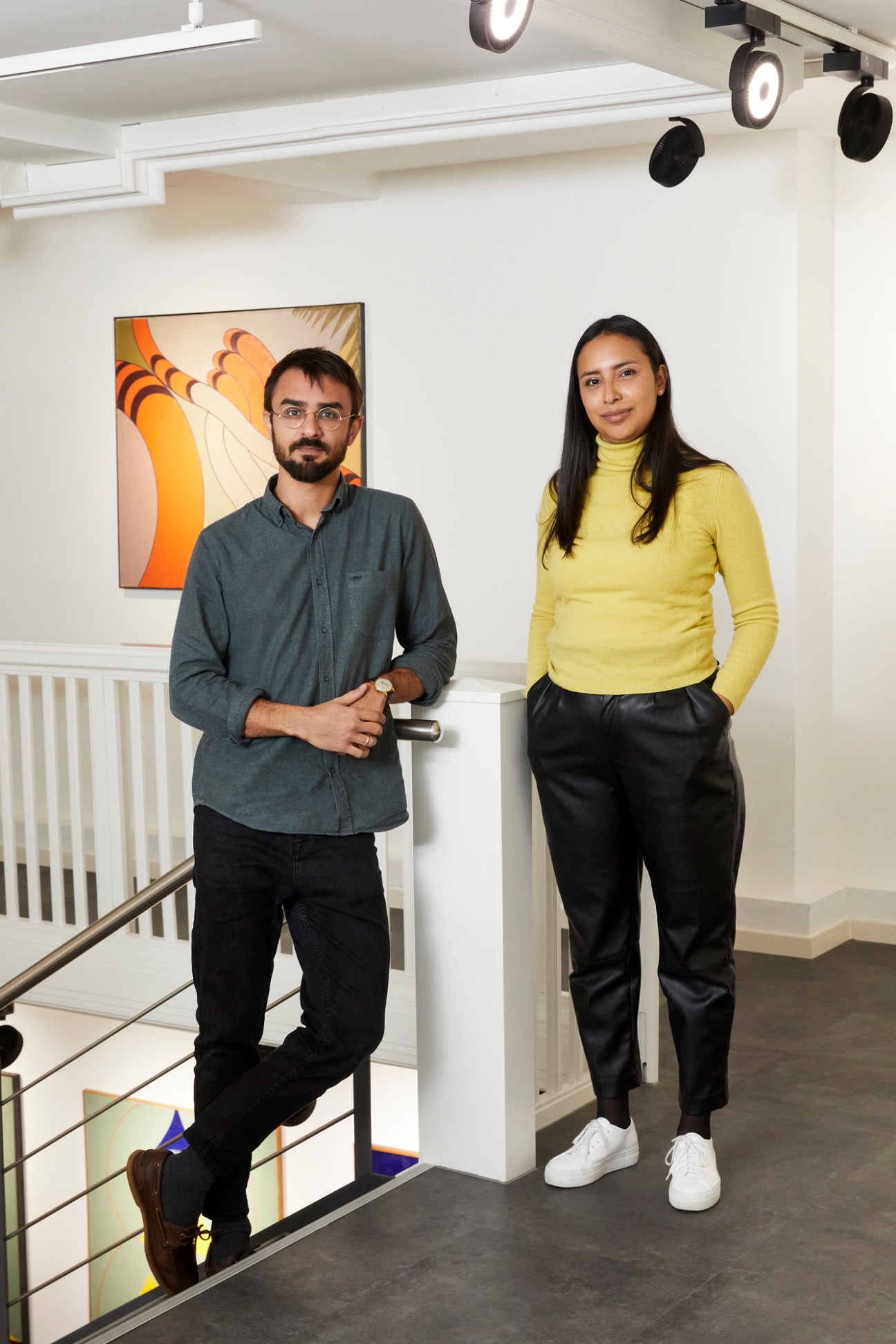 Gonzalez and fellow director Pier Stuker standing in modern gallery with track lighting and artwork