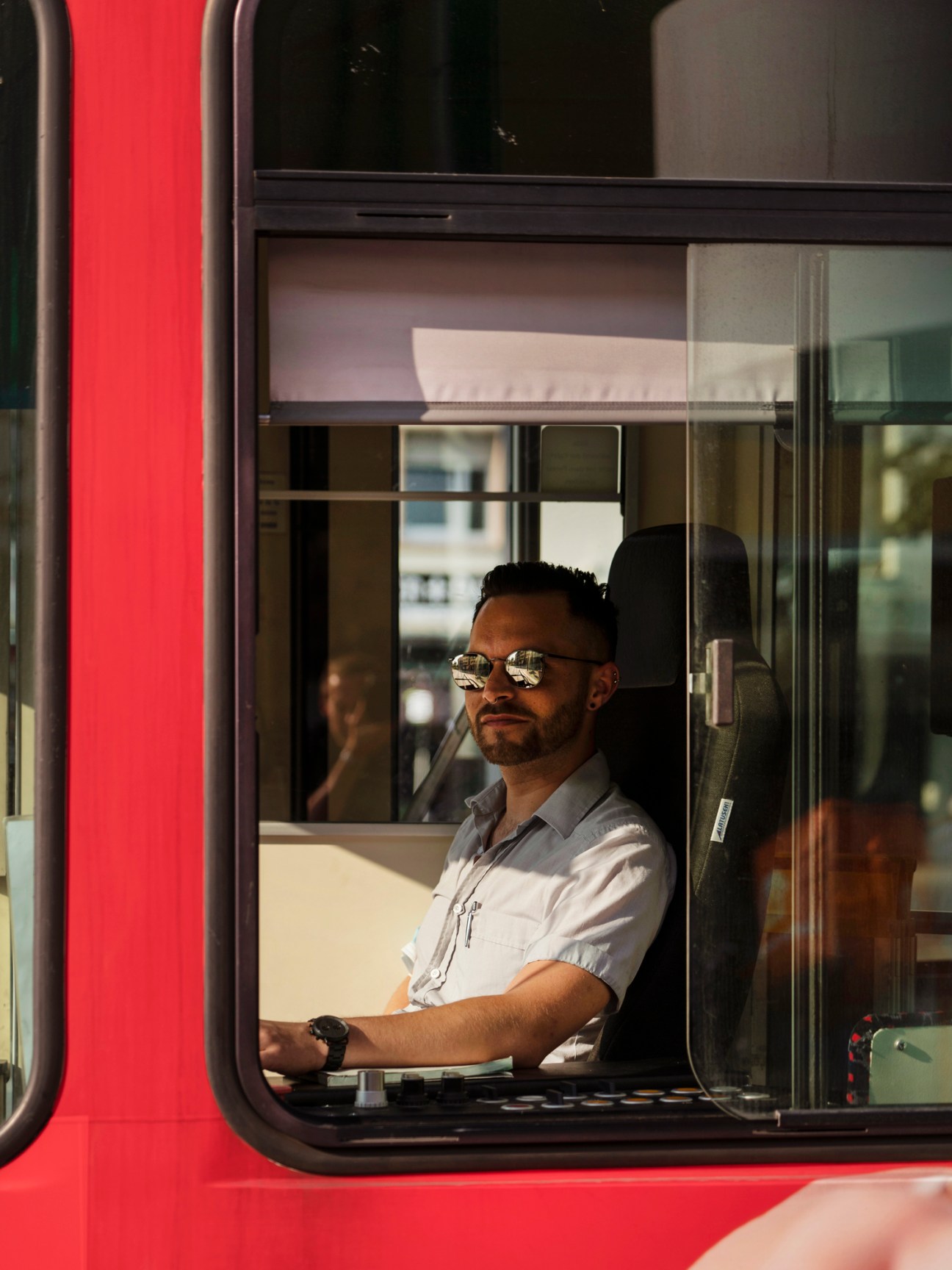Man in sunglasses and light shirt sitting in driver's seat of red public transport vehicle