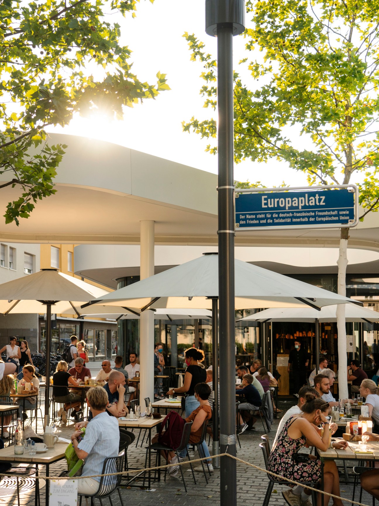 Outdoor dining area with people at tables under umbrellas at dusk
