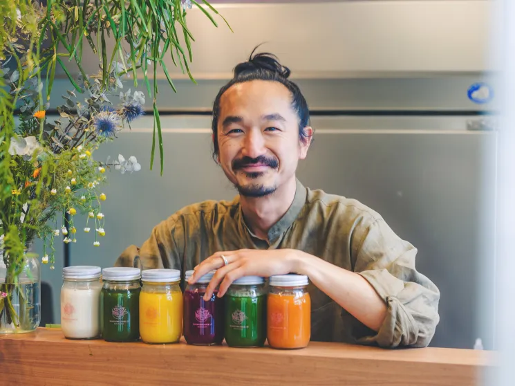 Man smiling behind a row of colourful jarred products on a counter.