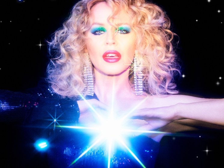 Glamorous performer with blonde curls and rhinestone earrings over lights.