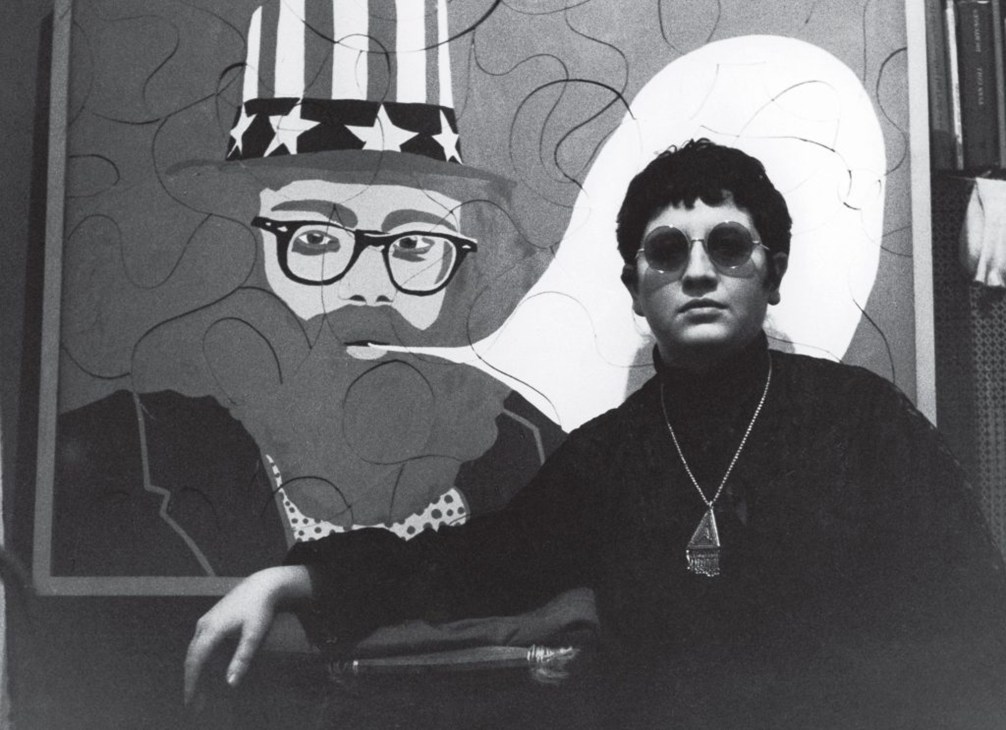 Black and white photograph of person wearing sunglasses and hat next to Uncle Sam artwork