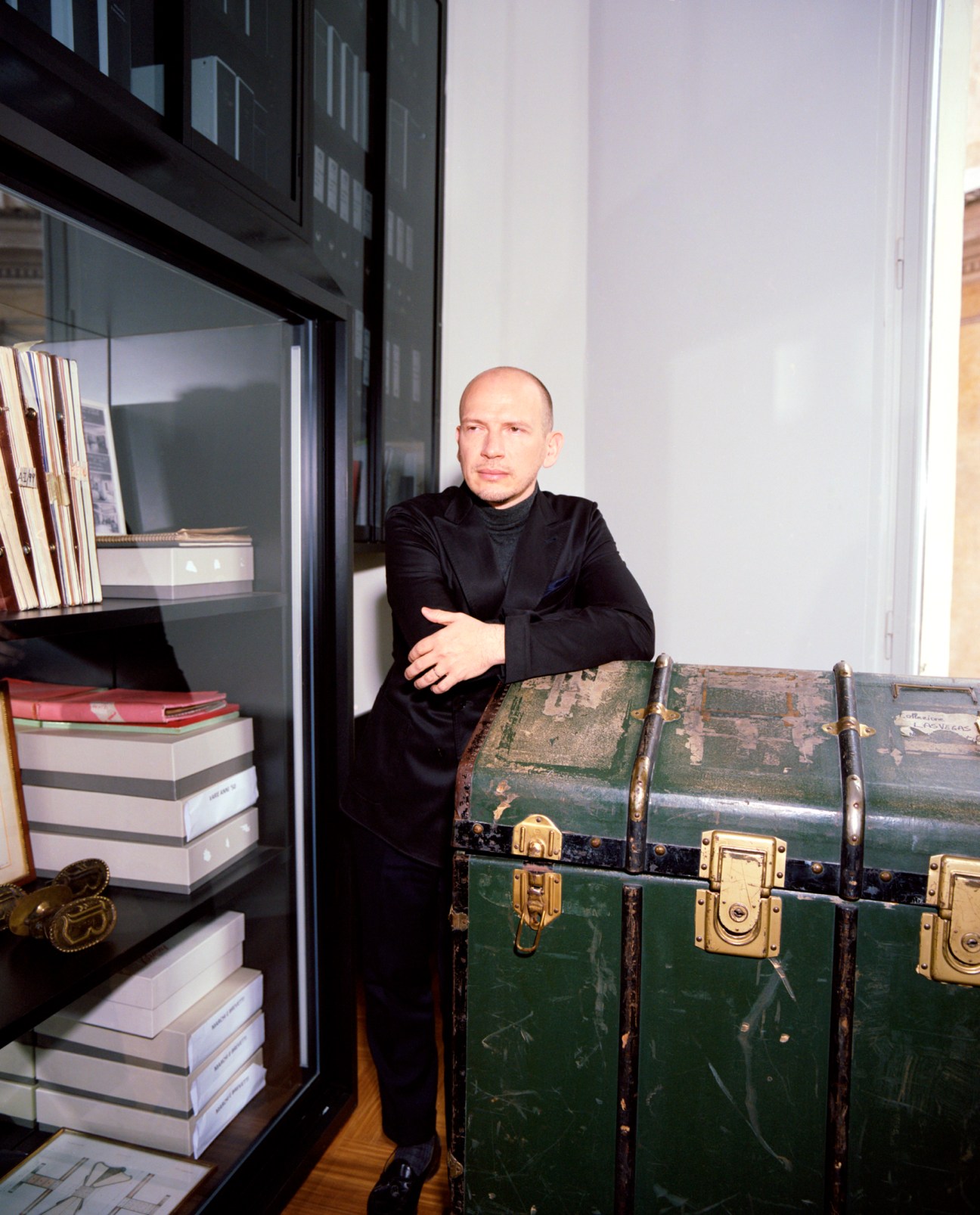 Norbert Stumpfl dressed in black standing with arms folded next to bookshelf