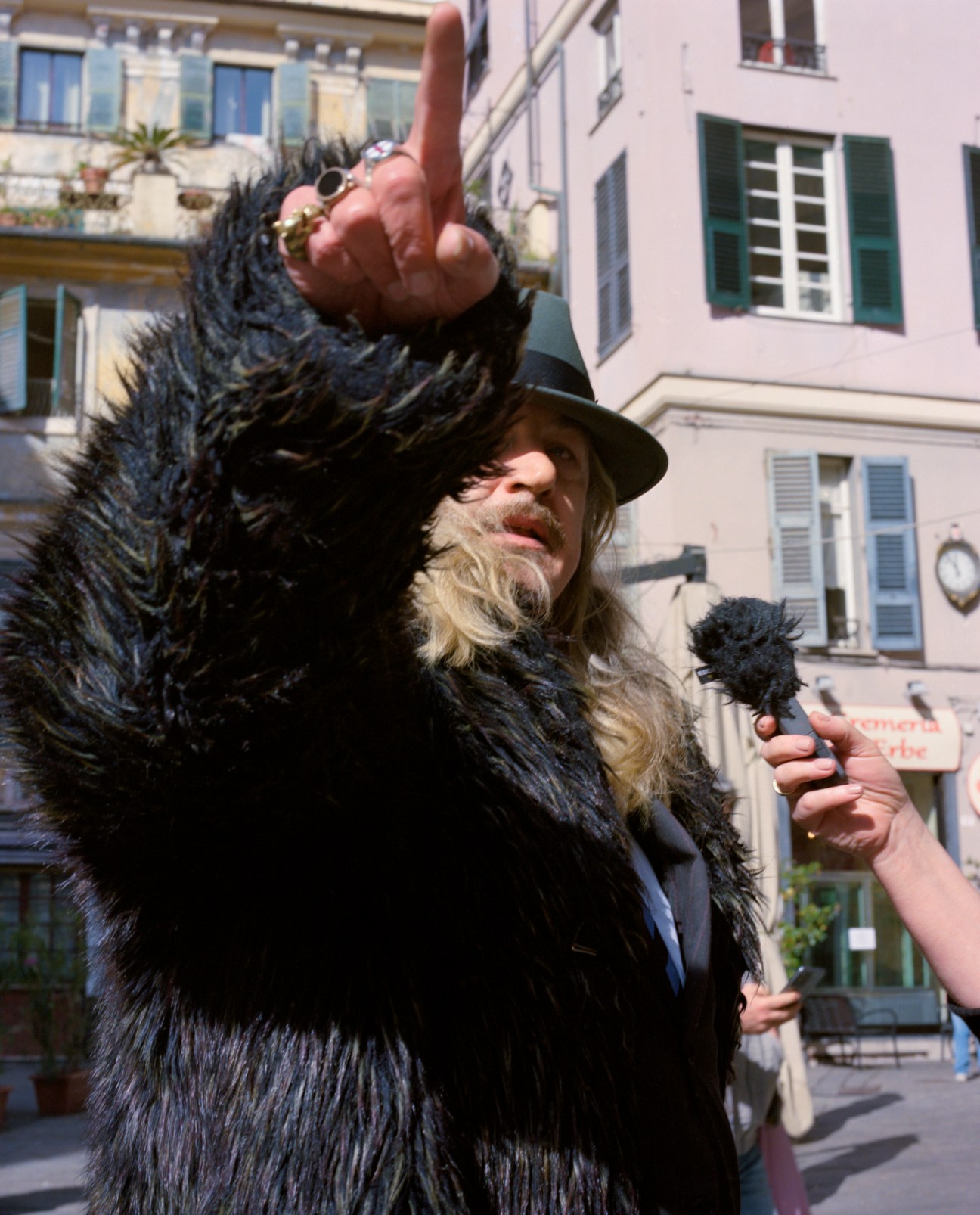 Ilja Leonard Pfeijffer gesturing while standing in Piazza delle Erbe in Genoa, pointing out architectural landmarks