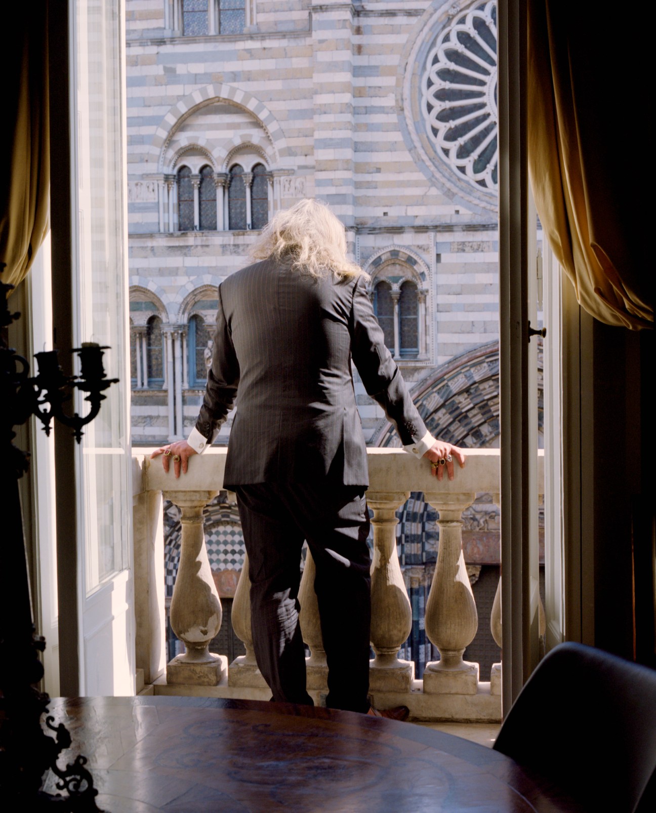 Man in suit standing on balcony overlooking historic striped cathedral architecture
