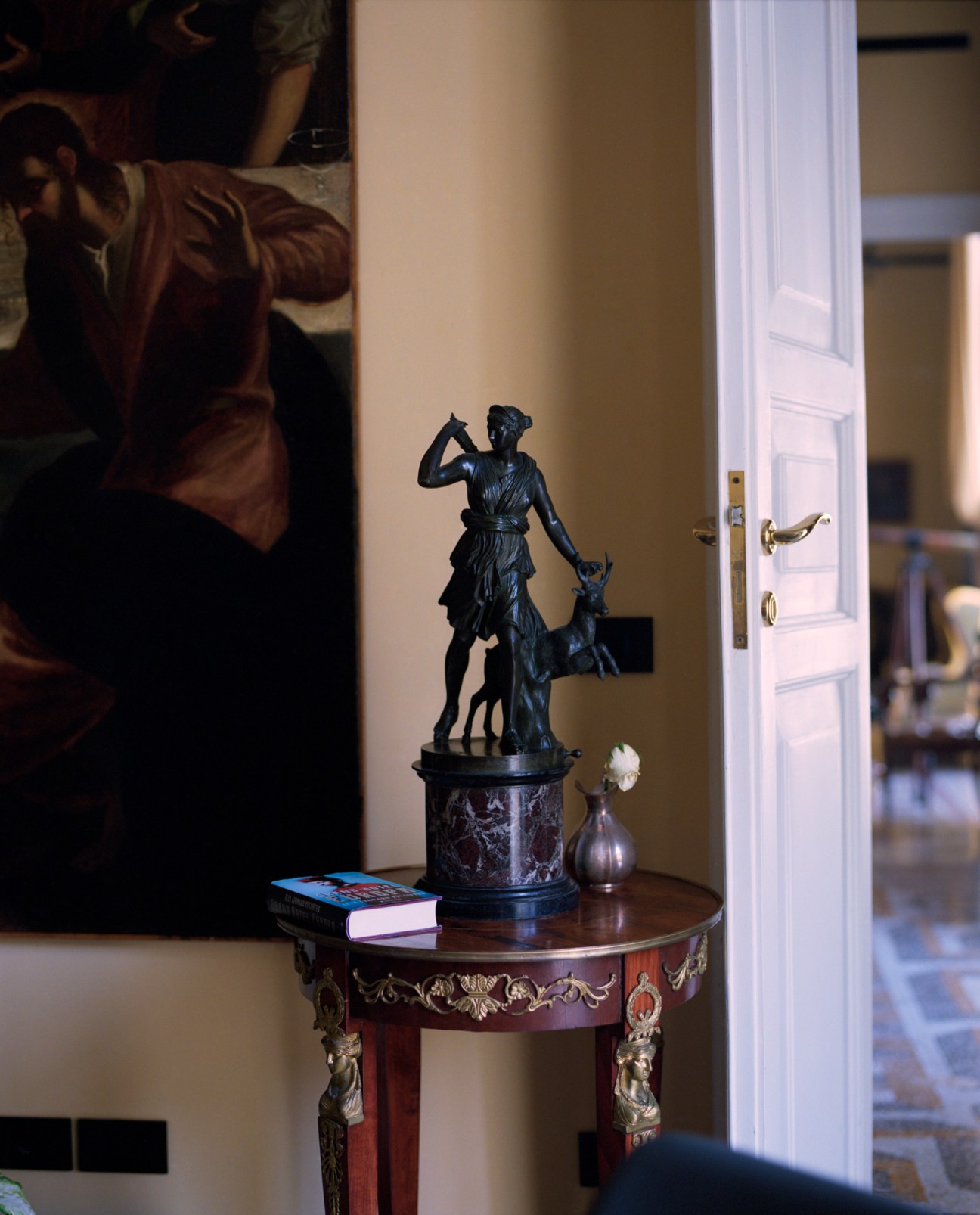 Bronze statue of Artemis with dog on ornate pedestal, displayed on decorative wooden table in elegant interior