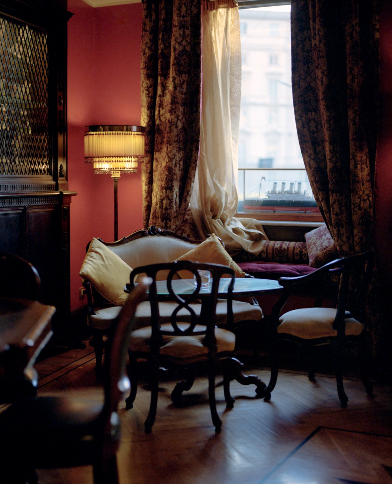 Elegant hotel room interior with period furniture, ornate curtains, and view of ship through window