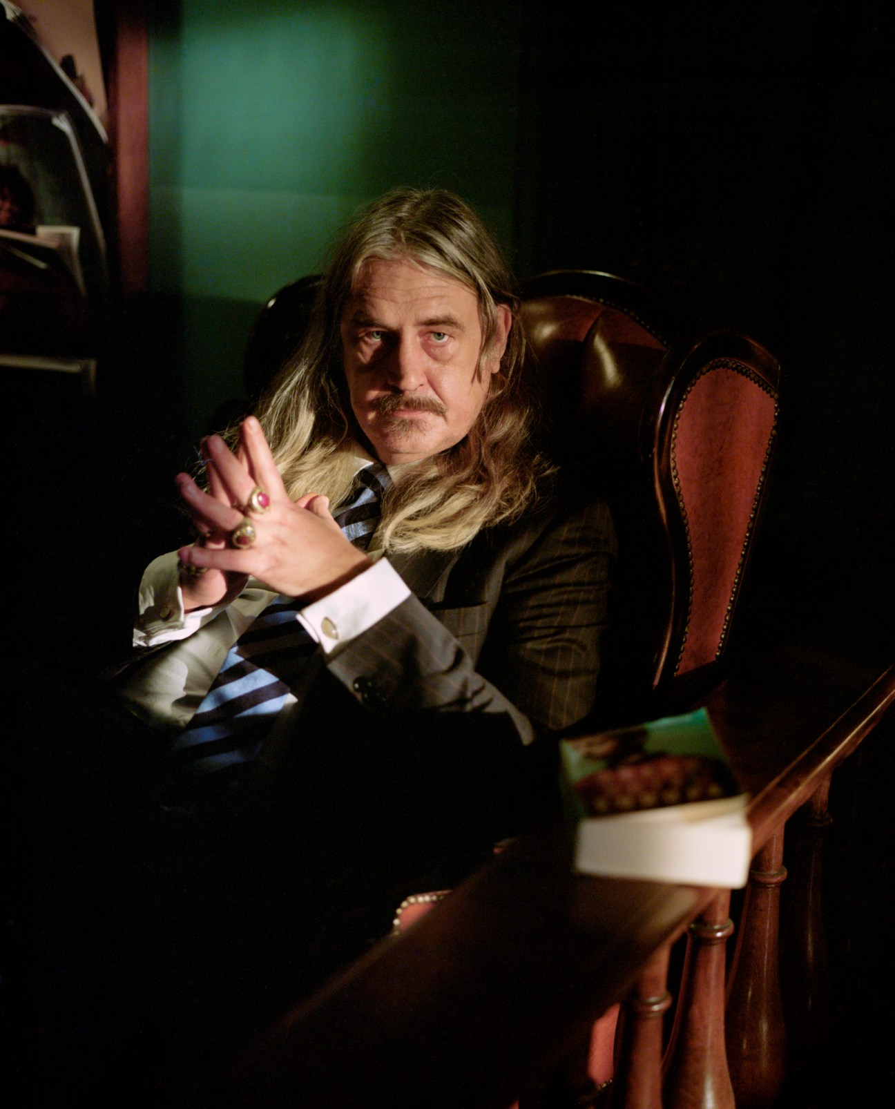 Ilja Leonard Pfeijffer sitting in an ornate leather chair with his hand raised, in an elegant hotel interior