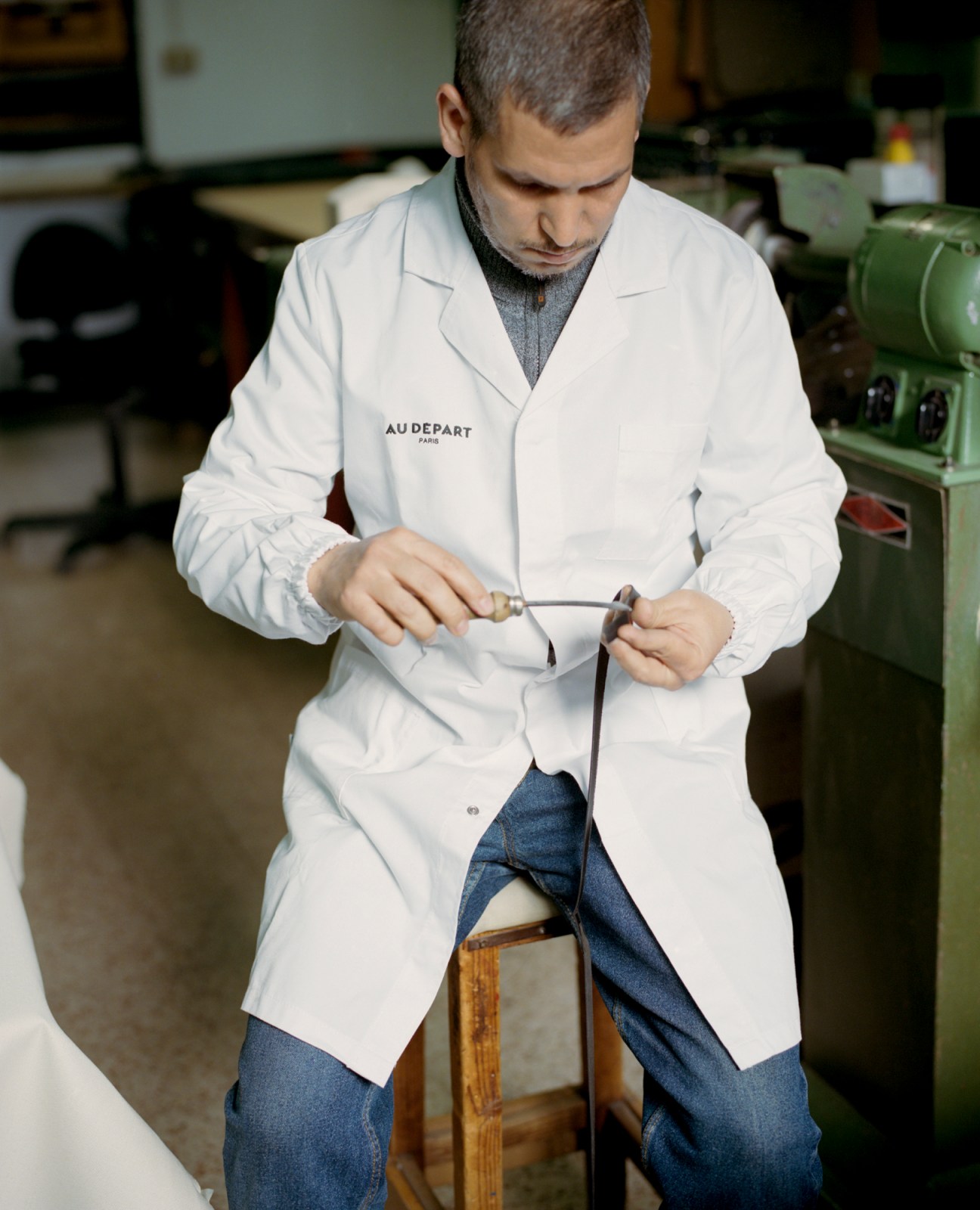 Artisan in white lab coat working on detailed craftswork at Au Départ's Milan workshop